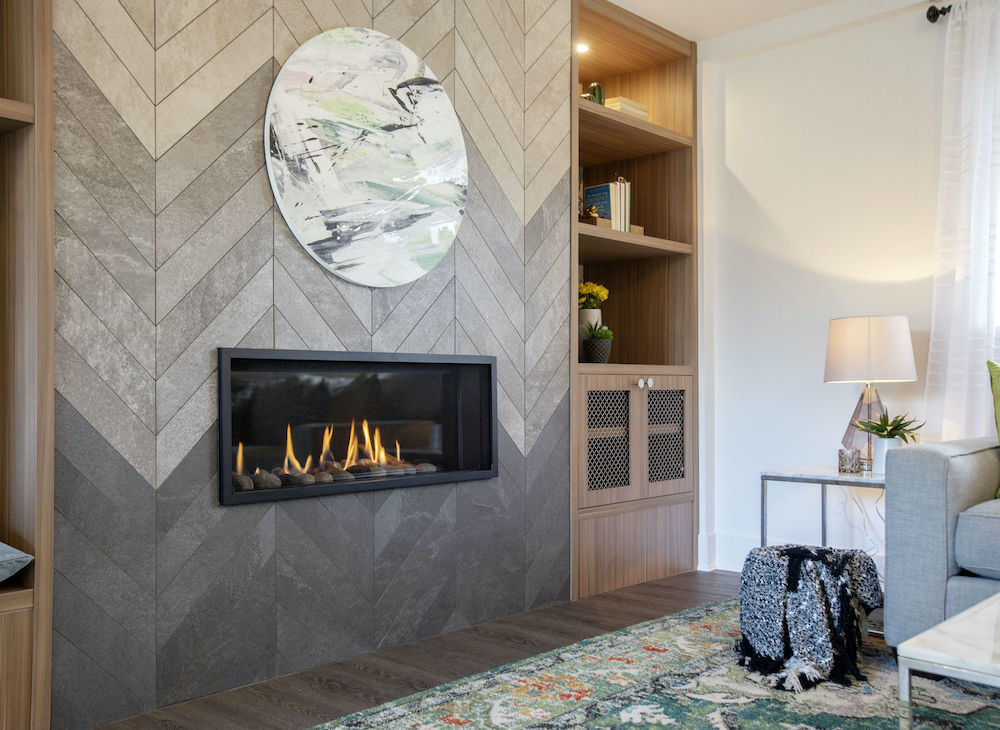 Chic living room with a long gas fireplace set into a feature wall with grey herringbone tile in an ombre pattern, dark wood floors, and built-in shelves as featured on HGTV’s Worst to First
