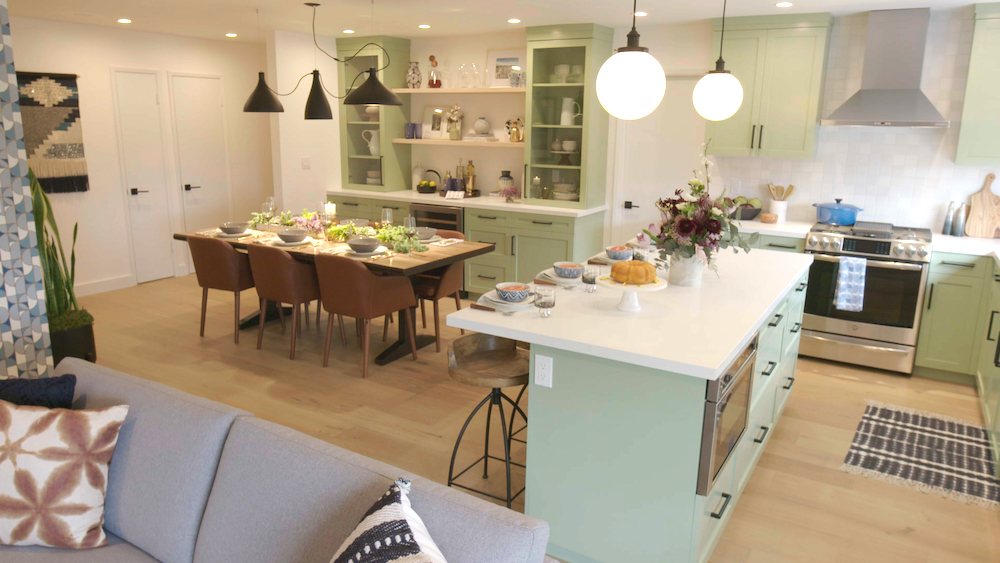 Cool modern kitchen with mint green cabinets, a kitchen island with two round pendant and a wooden dining room table