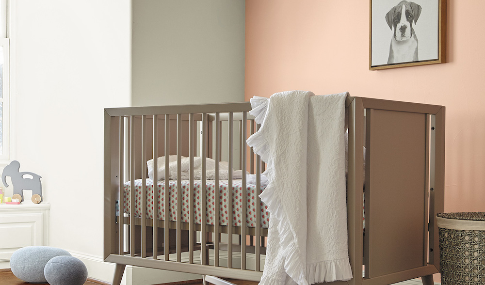 Sweet nursery with large light-filled window, grey wood crib with white sheets, a wall painted in BEHR Fruit Salad M200-2 with a framed picture of a puppy, and another wall painted in BEHR Silky White PPU7-12