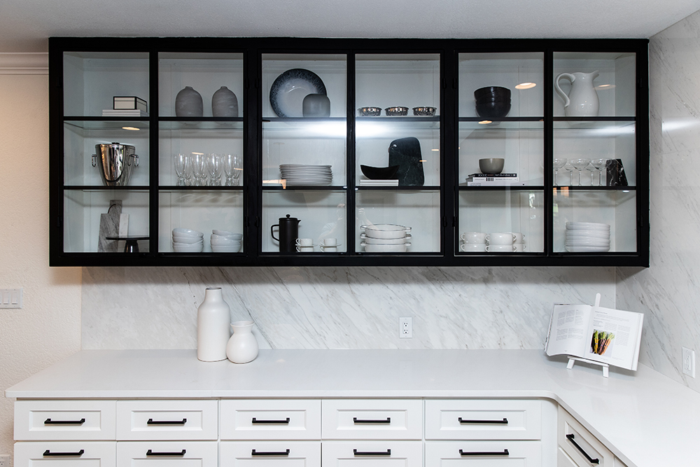 Large black crockery display case in a chic white kitchen with white cabinets with black handles and a grey and white porcelain backsplash