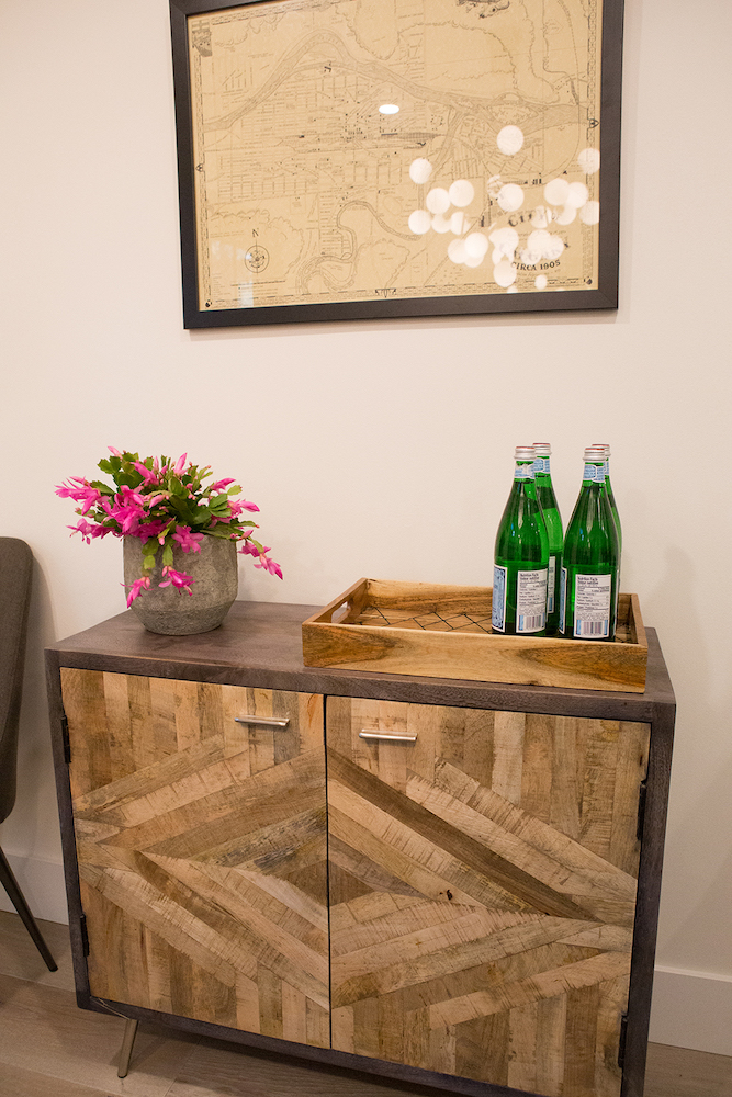 Chic mid-century modern inspired wood sideboard with inlaid doors topped with a potted plant, a try with bottles of San Pellegrino water, and a framed vintage map as featured on The Property Brothers on HGTV