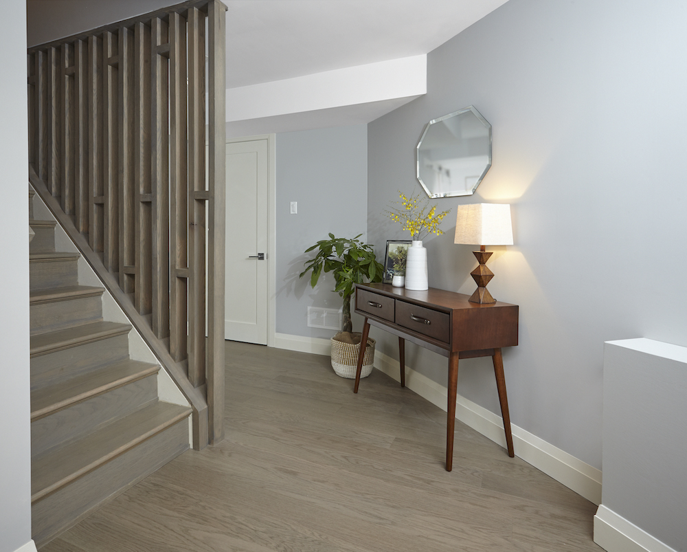 Basement hallway with a set of stairs, customized wooden railing wall, and a hall table with a wooden lamp and mirror