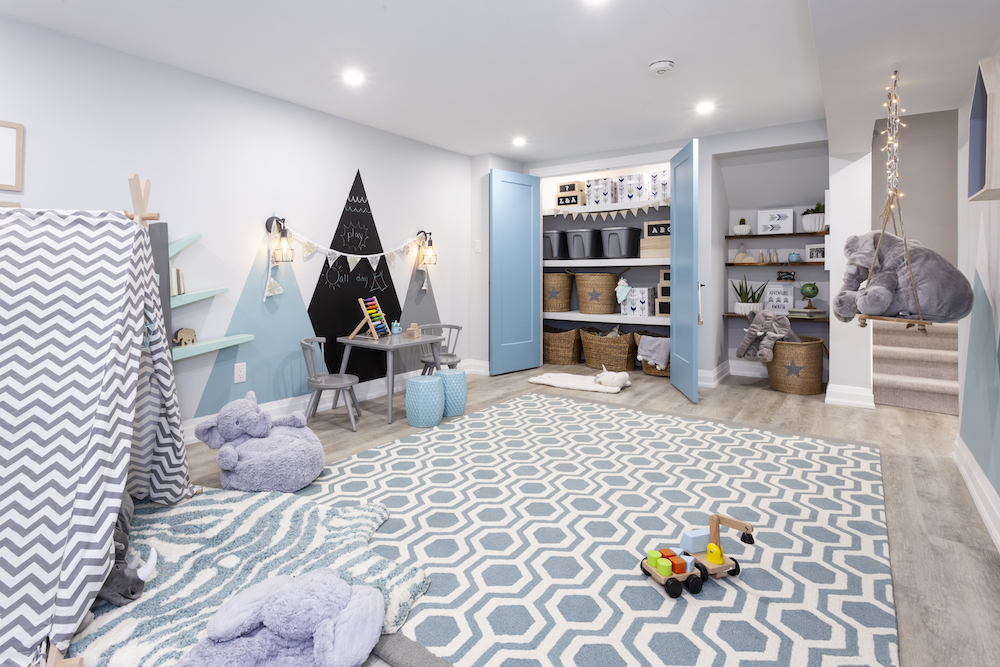 Chic basement playroom with a mountain mural on the wall, a large blue patterned rug, a grey play table and two chairs, a chevron play tent and a large toy closet
