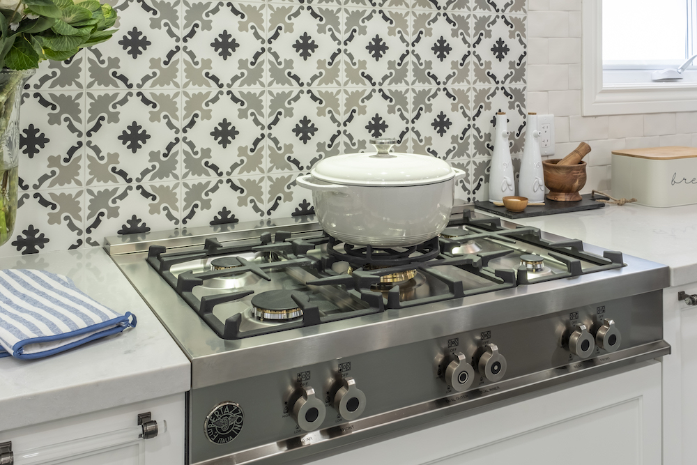 Stainless steel stovetop with a grey and white tiled backsplash and large white pot