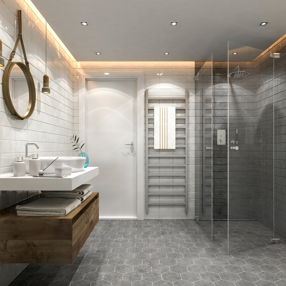 Chic modern bathroom with grey hexagon floor tiles, a wall ladder towel warmer, a walk-in shower with glass doors, and a round wall mirror above a floating ceramic and wood vanity with a vessel sink, folded towels and accessories