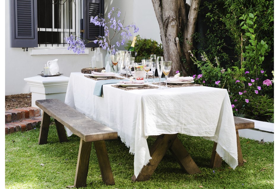 Simple white linen on a rustic outdoor table with glassware on top