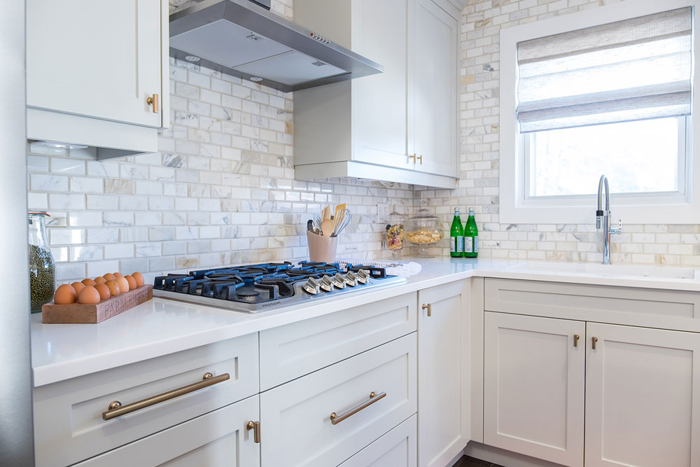 White kitchen with brick subway tile and brass hardware.