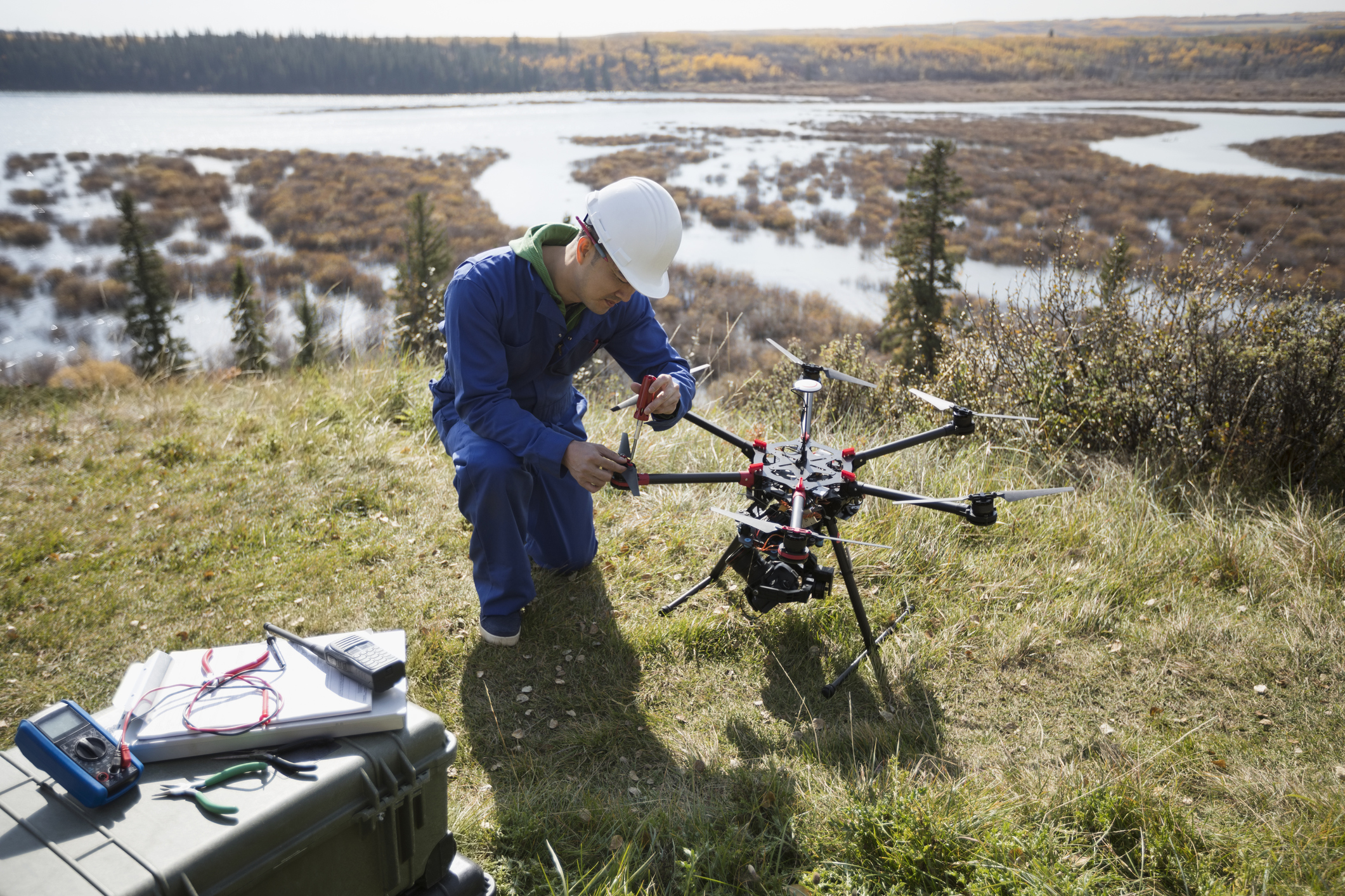 Surveyor repairing drone equipment on hilltop overlooking lake