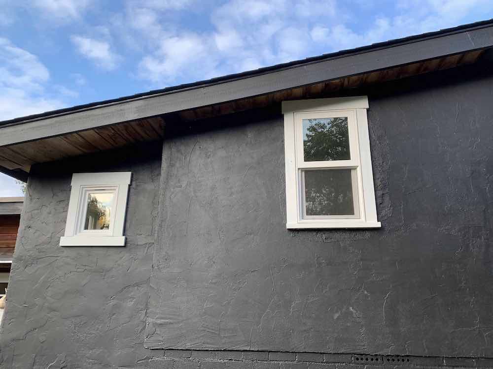 Exterior of a cottage against a blue sky with walls painted black with BEHR Black Smoke PPH-34 and window trim painted with BEHR Ultra Pure White 1850