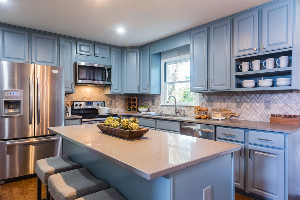 Modern blue kitchen with large island and chevron backsplash.
