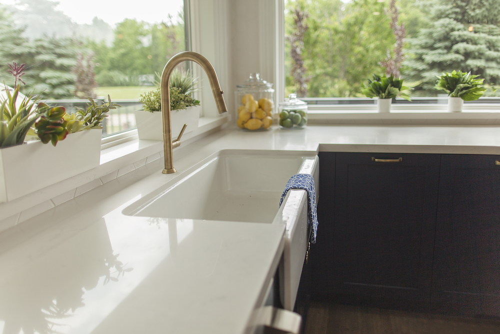 Shiny white countertops and a deep sink with a gold faucet in a large modern kitchen