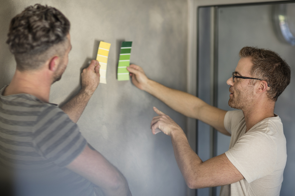 Two men holding colour swatches against bare grey wall