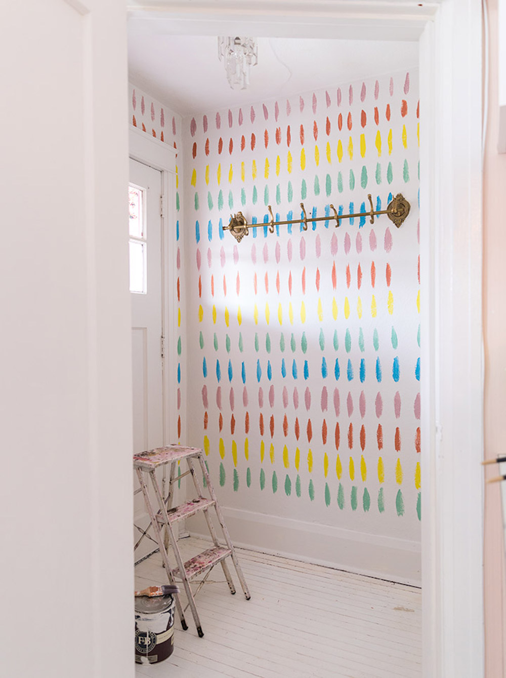 Colourful rainbow lines painted on a white wall in an entryway as part of a DIY project by HGTV’s DIY expert Tiffany Pratt
