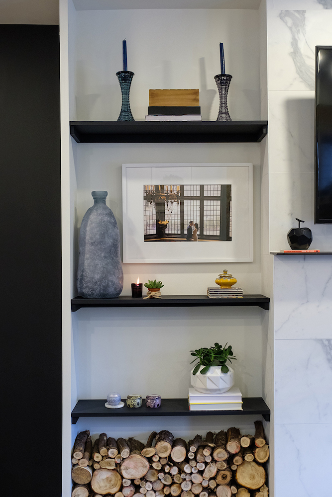 A built-in shelf holds firewood, a white succulent planter, a framed wedding photo, a large ceramic vase and candles