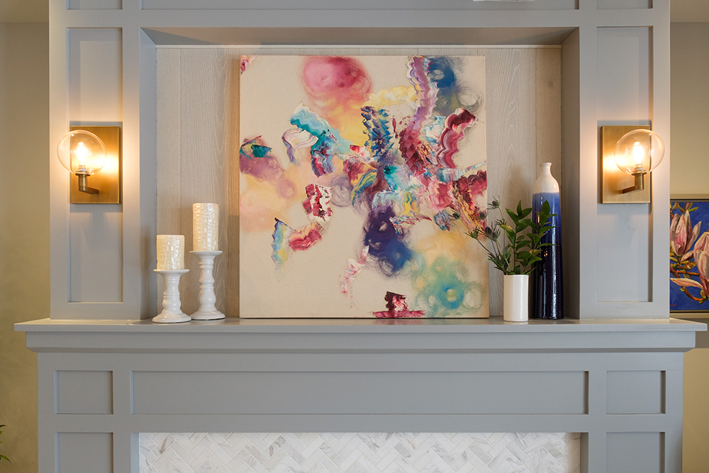 Grey wood moulding create a unique mantle to display white candles and a colourful painting