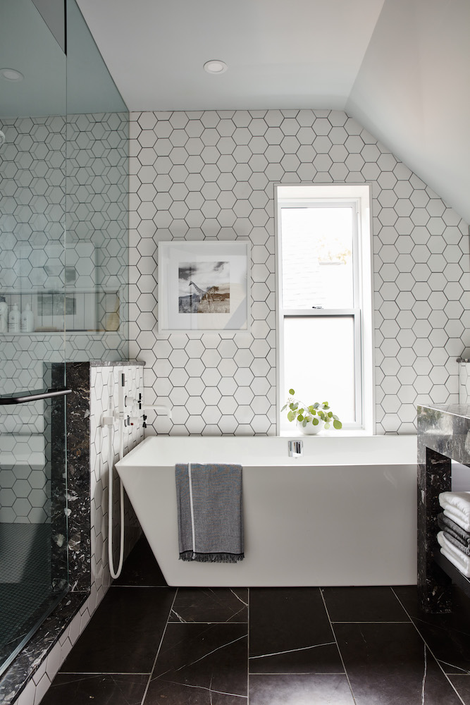 A chic modern bathroom with a deep soaker tub, black floor tiles, white hexagon wall tiles and walk in shower