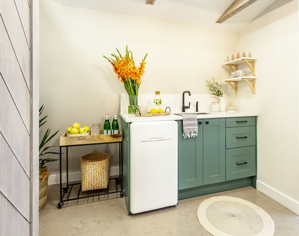 Cute kitchenette with a small white fridge, a wooden drinks cart and green cabinets