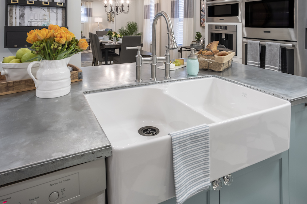 A white double sink sits on a kitchen island with a natural zinc countertop