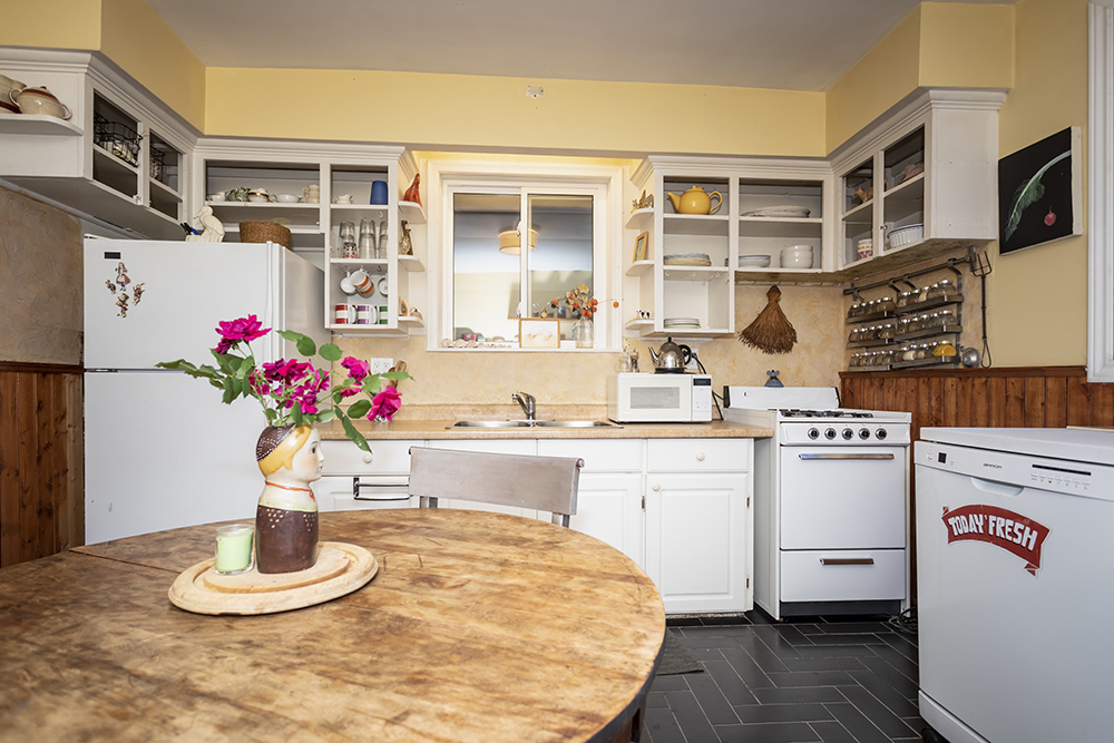 Old kitchen with round dining table, white cabinets and tired appliances