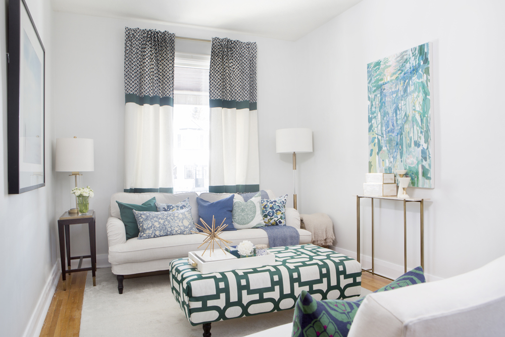 white living room with white and green patterned drapes, ottoman and green and blue abstract