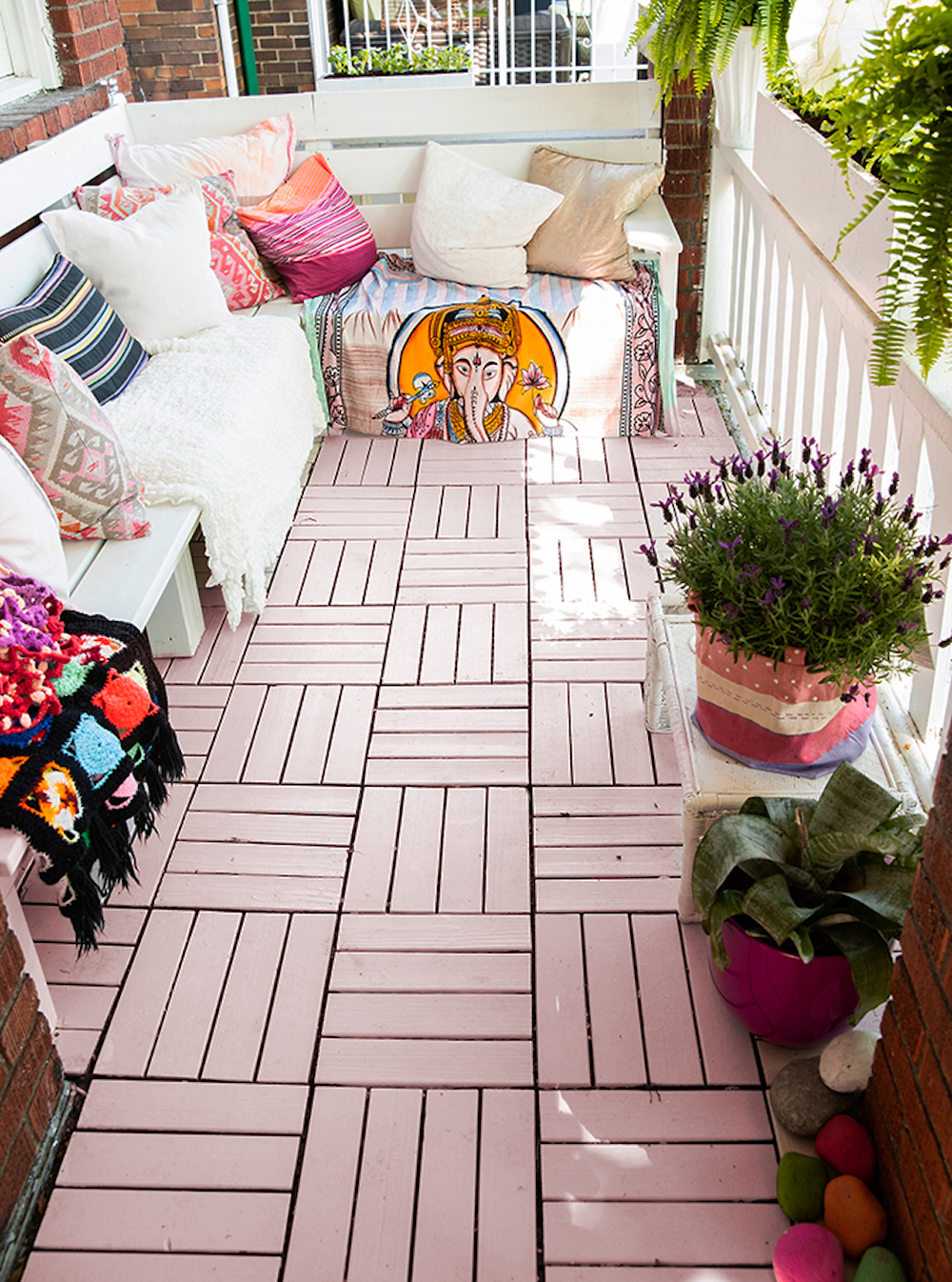 Pink patio floor tiles feature on a revamped back deck with a white built in bench covered in colourful cushions designed by Tiffany Pratt for HGTV