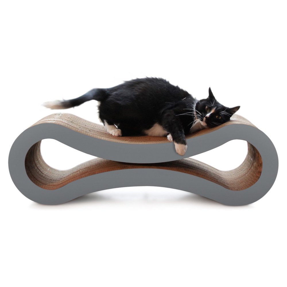 Black and white cat lounges on a grey carboard cat lounger