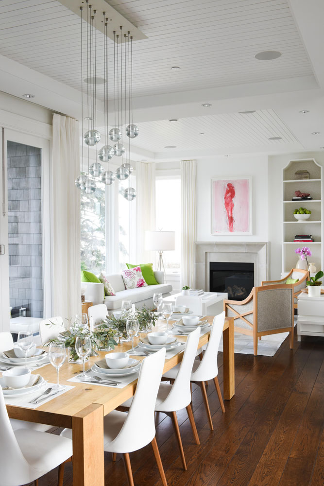 dining room with wood table and white chairs looking into living room with pink painting over fireplace