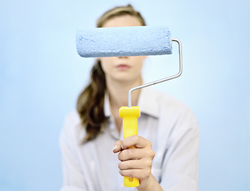 Young woman holding paint roller in front of her face