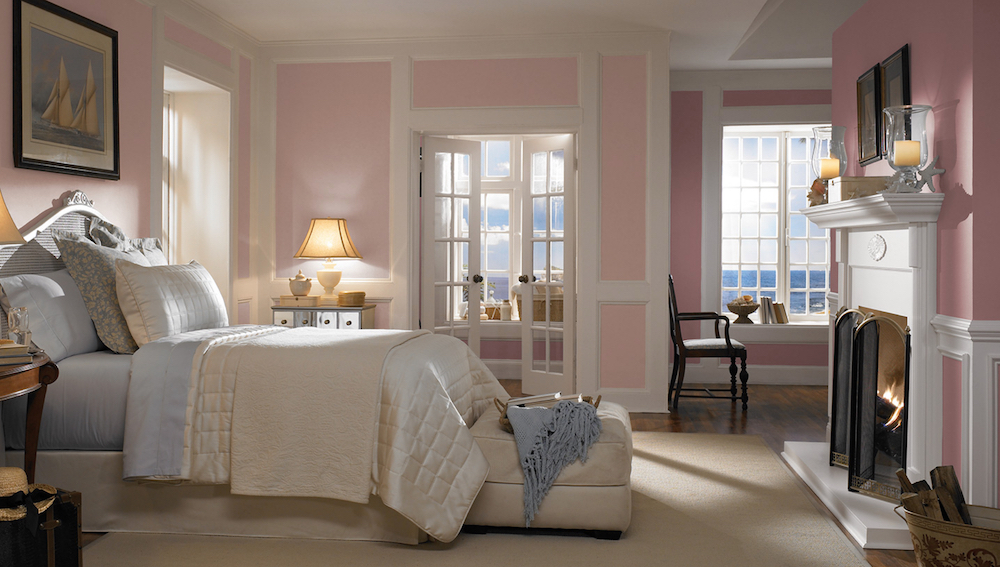 Pretty pink bedroom with large bed made up with blue and white bedding, an open fireplace, and walls painted in BEHR Moxie MQ3-35, Polar Bear 75 and Mauve It N120-3