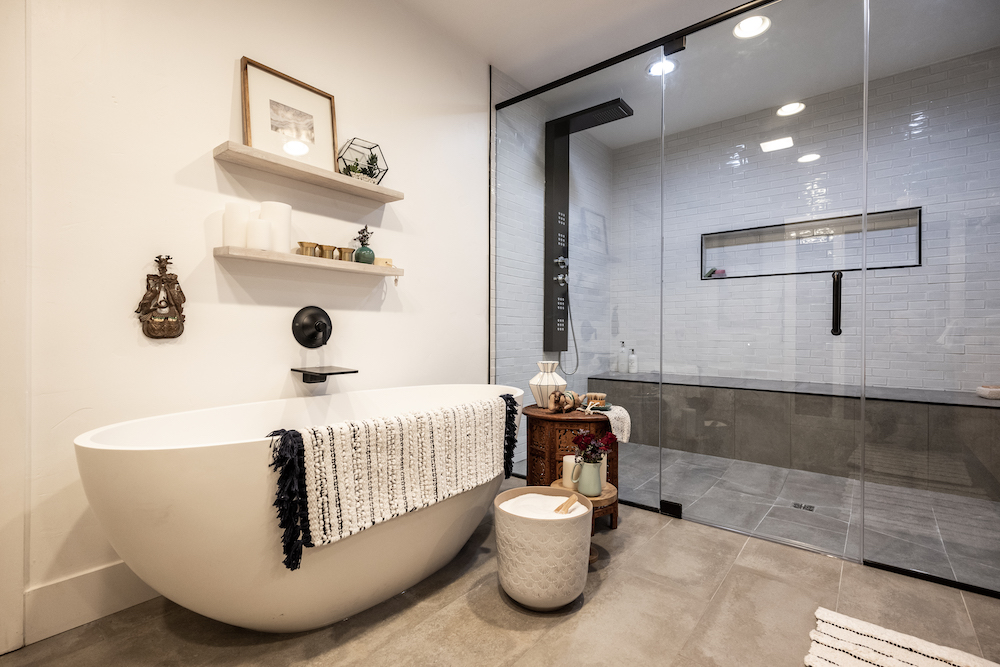 Modern bathroom with egg-shaped freestanding tub, large walk in shower, two floating wood shelves and sand-coloured floor tiles
