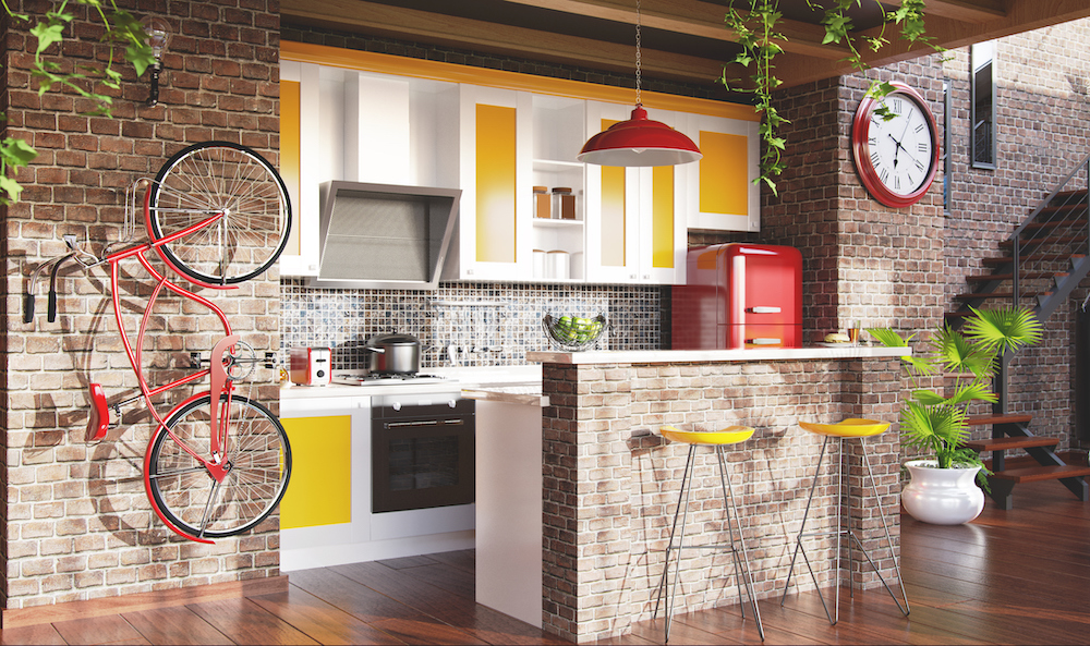 A colourful loft kitchen with exposed red brick walls, hardwood floors, yellow paint on the cabinets, a red fridge and pendant lamp, a red bike hanging on the wall and a large red clock at the base of a set of metal stairs