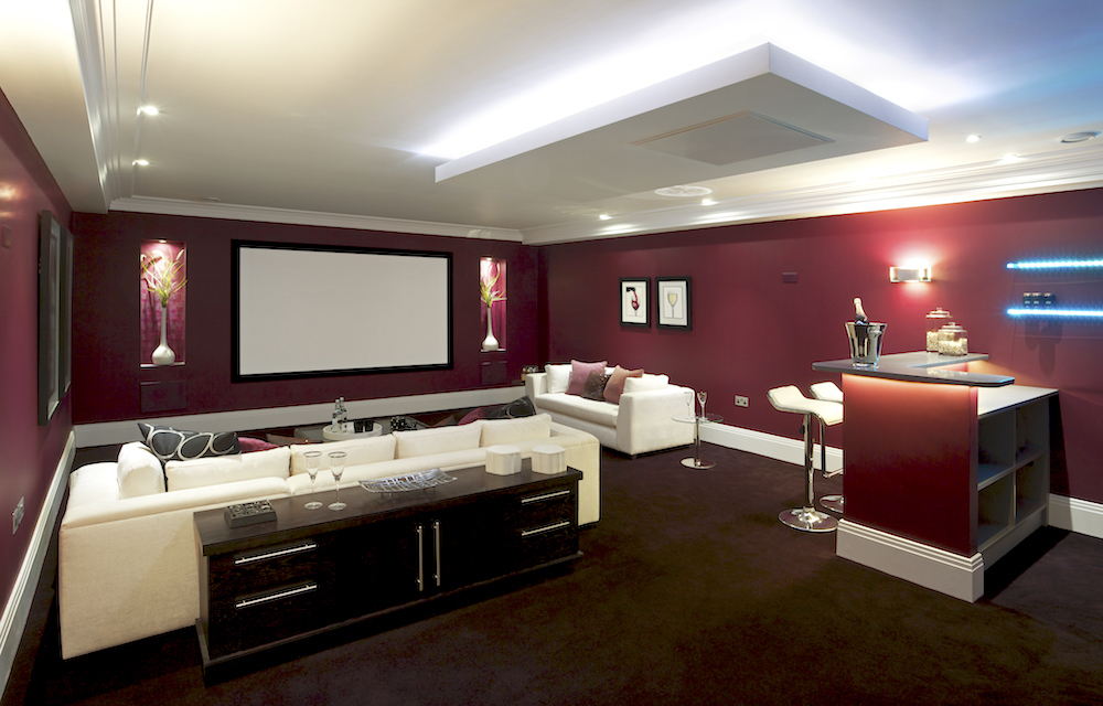 A beautiful cinema room in a luxury new home with two white couches facing a large viewing screen