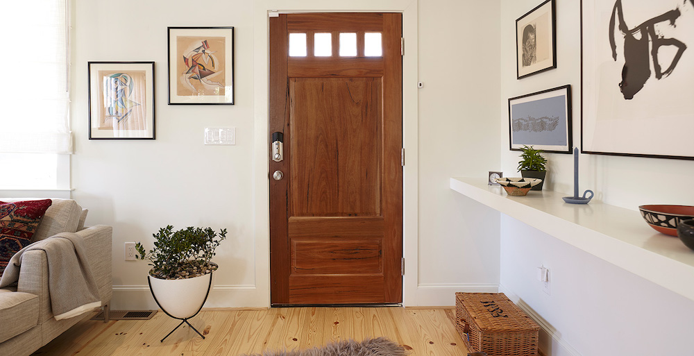 A clean and welcoming entry features a stained wood front door, framed modern art on the walls, a floating shelf with a bowl, plant and candlestick, a potted plant on the floor, and white BEHR Polar Bear 75 paint on the walls.