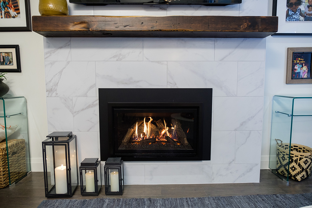 Chic family room with white marble tiles surrounding a gas fireplace and wooden mantle