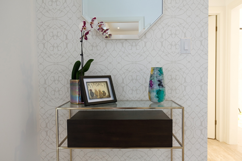 A gold glass topped hall table displays a family crafts project, an orchid and a colourful glass vase