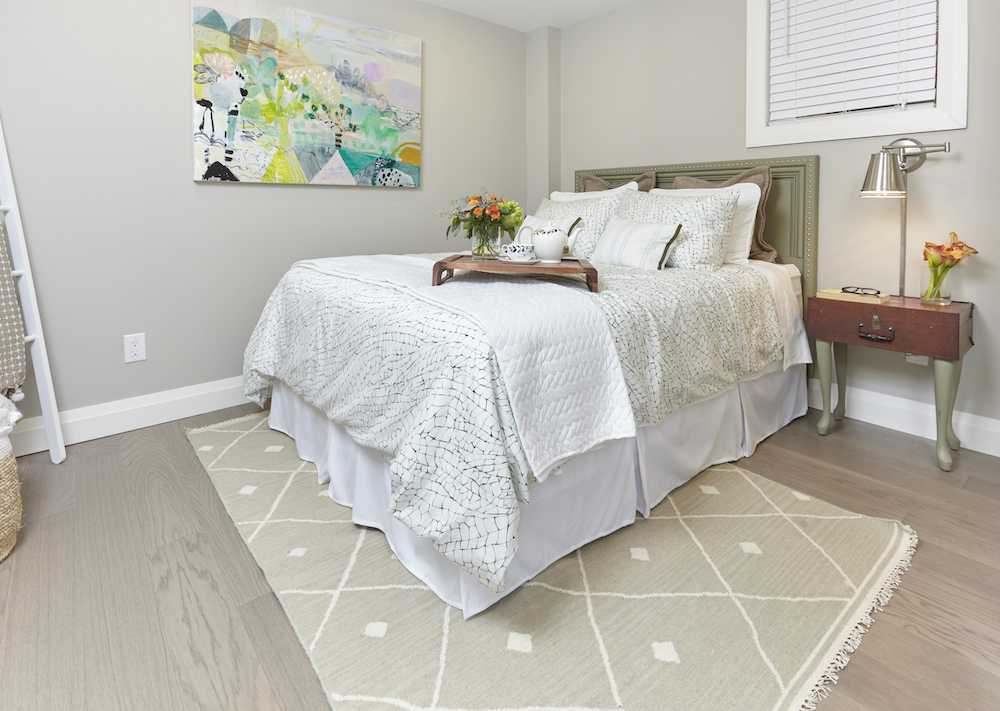 Modern guest bedroom in a finished basement with a diamond patterned beige rug, antique box side table and a bed with a green headboard