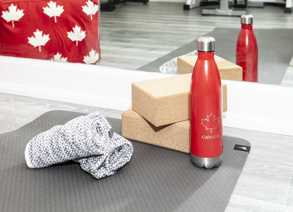 A grey yoga mat sits in a new basement gym with a red water bottle, two grey workout towels and two yoga cork blocks