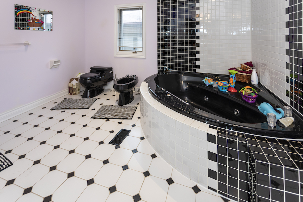 An old 1980s black jacuzzi tub surrounded by black and white tile and a black toilet and bidet set