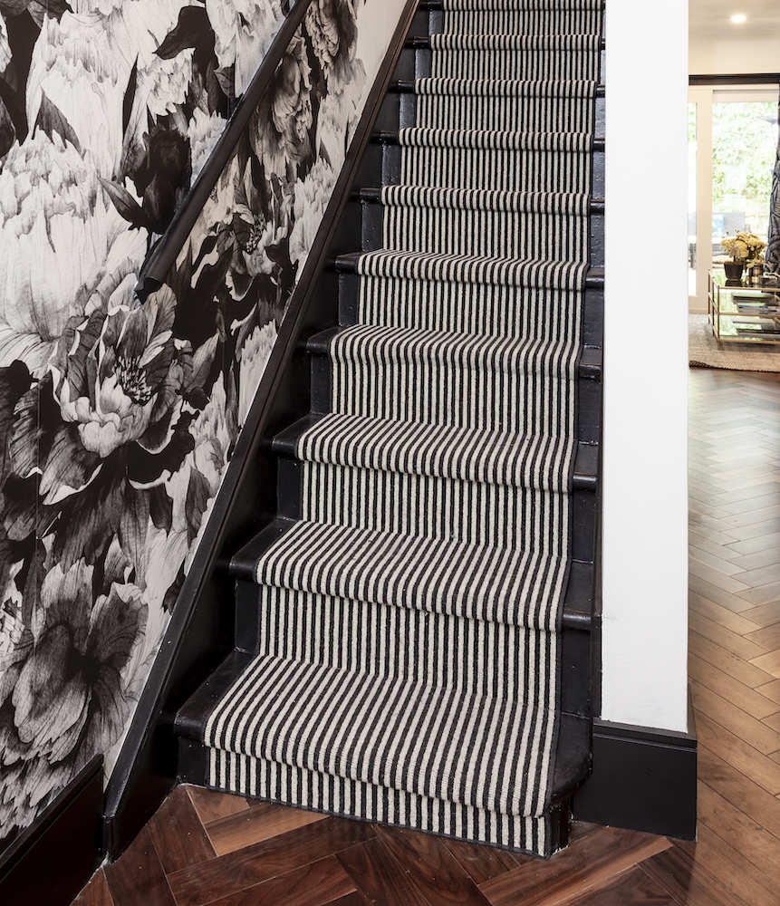 Black staircase with a black and white striped runner and a wall covered in a black and white floral wallpaper