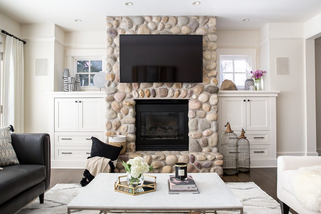 full on view of round stone fireplace with tv above and flanking white cabinets