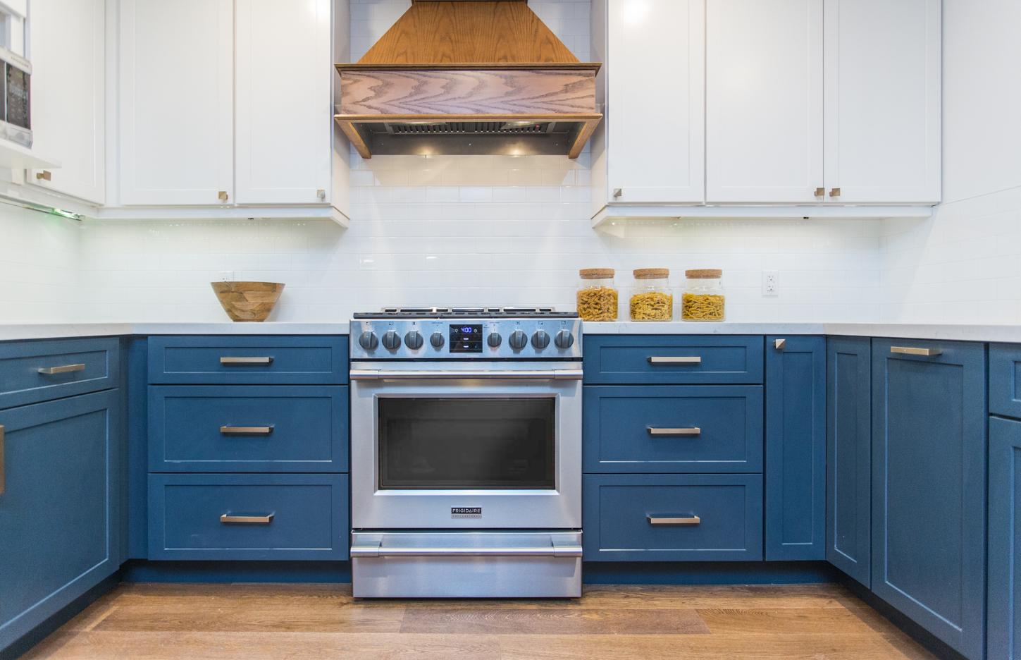 The rich blue of the lower cabinets grounds this custom cook’s kitchen, while the matching wooden hood vent and hardwood flooring creates a cohesive design aesthetic.