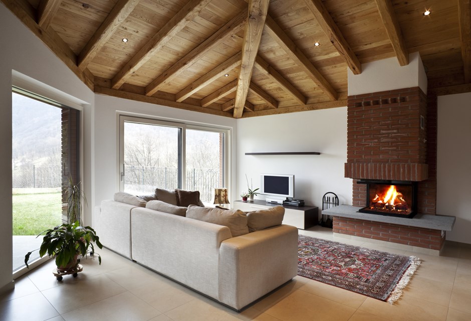 A spacious cottage living room with beige couch, exposed beams and roaring fire in the fireplace
