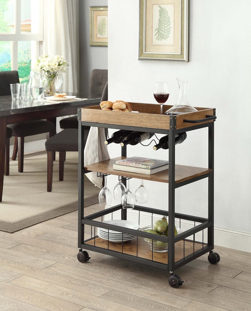 Rustic industrial kitchen cart with three wooden shelves stacked with white plates, a bowl of pears, cook books, wine glasses and wine bottles