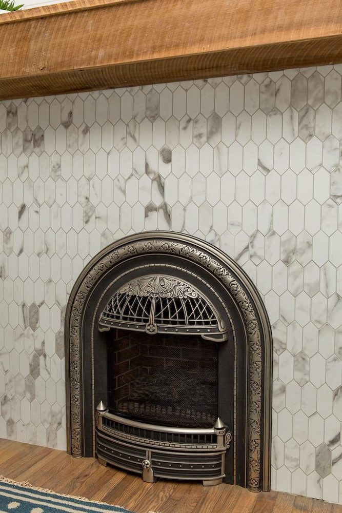 Funky art-deco gas fireplace insert surrounded by bright white-marble tiles and capped with a rustic, rough-wood mantel