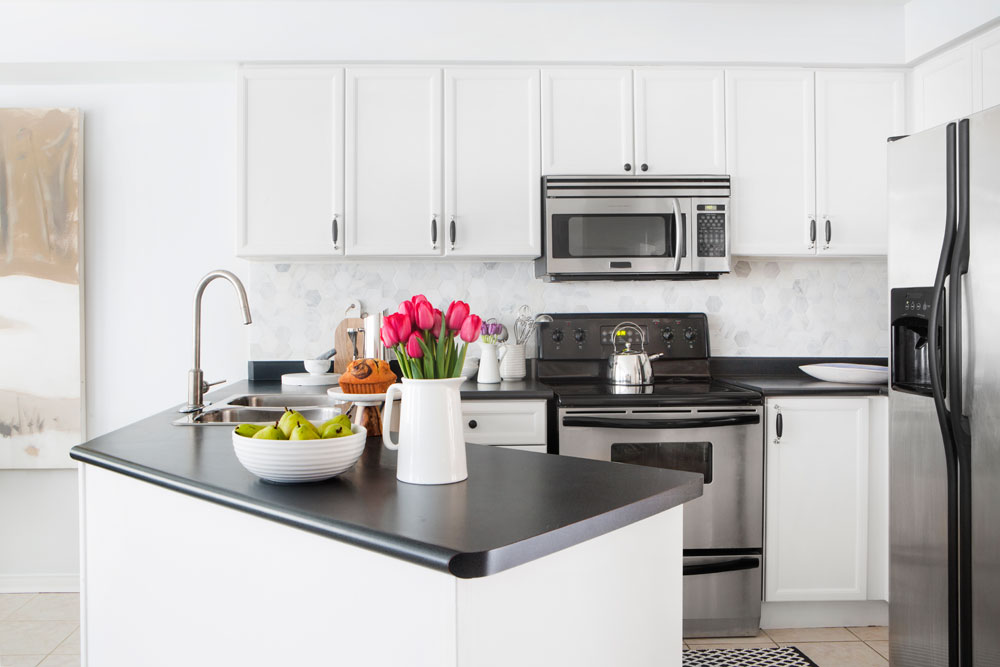 Small black-and-white kitchen with angled peninsula and black countertops.