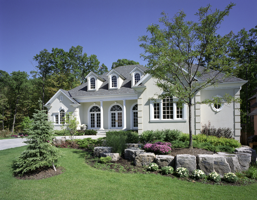 Pretty new white house with landscaped front yard features a rock lined garden bed and two young trees