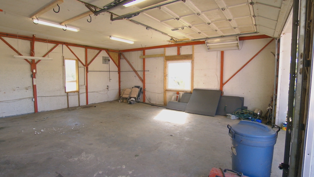 Rough interior of an old garage with a cement floor and blue bin