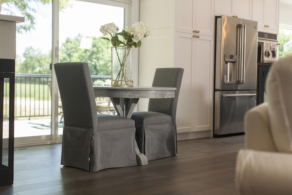 Two grey upholstered chairs sit at a small grey round table by a set of glass sliding doors