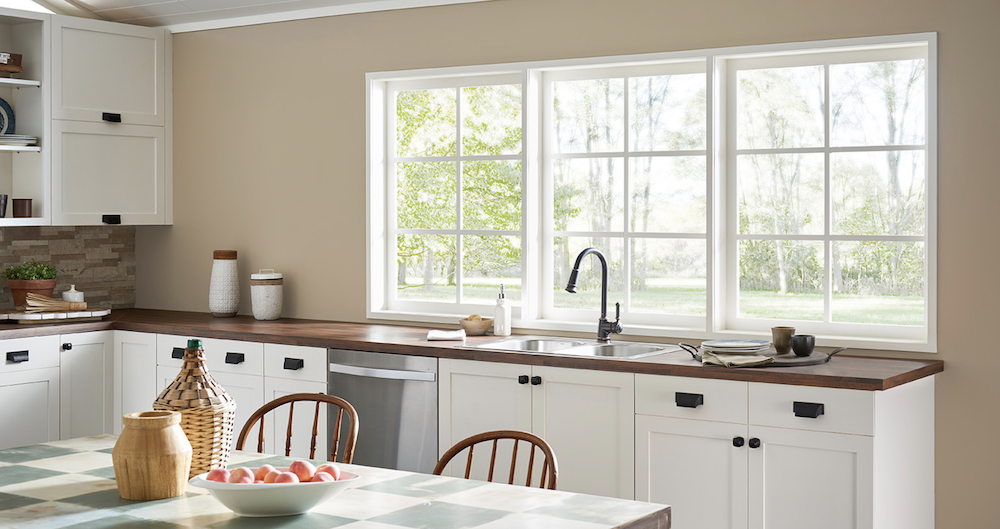 Pretty, traditional kitchen with three windows, wood countertops, beige walls painted in BEHR Hayloft MQ2-22, and white cabinets with black hardware painted in BEHR Swiss Coffee 12