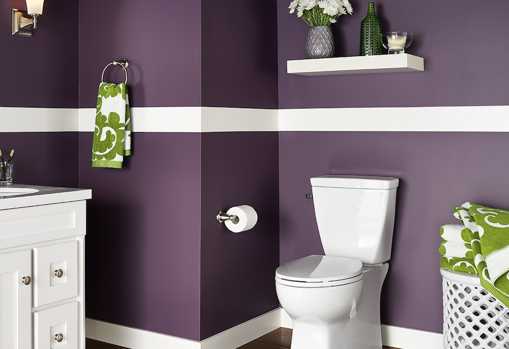 Small bathroom with a white toilet and vanity, and purple walls painted in BEHR Sultana P100-7 with a white stripe painted in BEHR Night Blooming Jasmine YL-W10